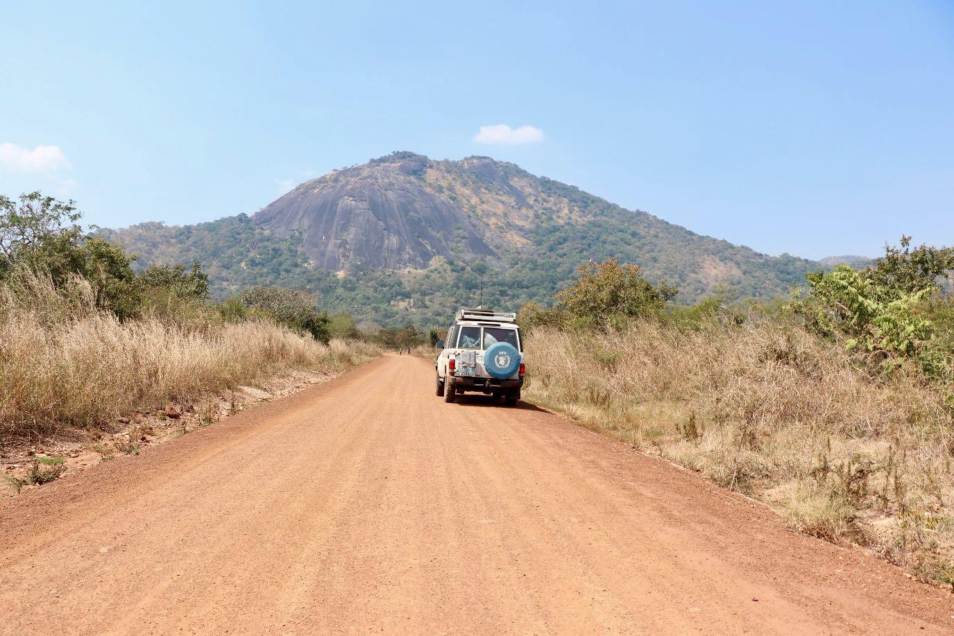 A vehicle travelling along an unpaved road towards hills